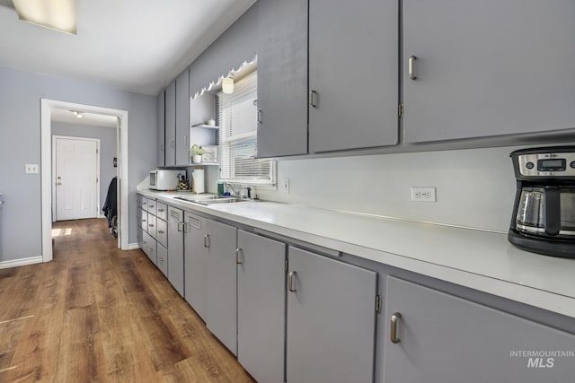 kitchen featuring a sink, open shelves, light countertops, gray cabinets, and dark wood-style flooring