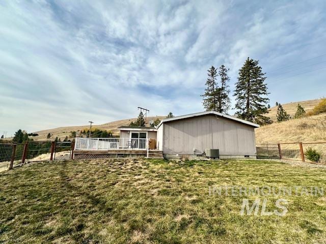 rear view of property with a wooden deck, central AC, a lawn, and a rural view