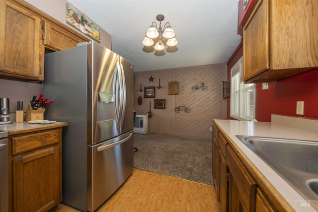 kitchen with stainless steel fridge, light wood-type flooring, brown cabinets, a chandelier, and wood walls