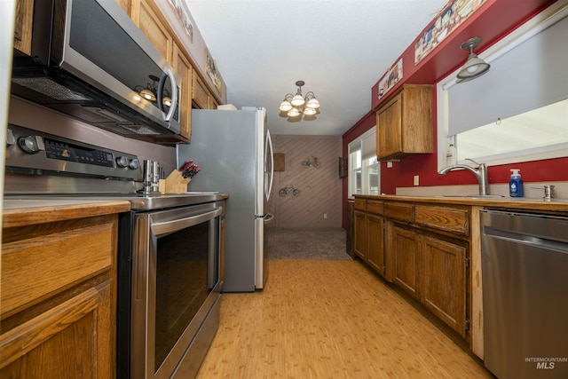 kitchen featuring stainless steel appliances, brown cabinets, a chandelier, light wood-style floors, and wood walls