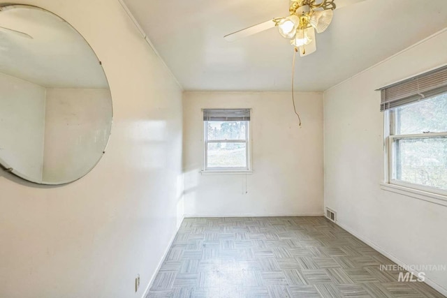 spare room with a wealth of natural light, light parquet floors, and ceiling fan