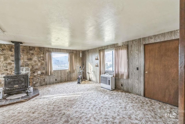 unfurnished living room with carpet flooring, a wood stove, and a textured ceiling