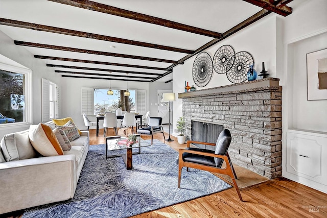 living room featuring beam ceiling, a stone fireplace, and wood-type flooring