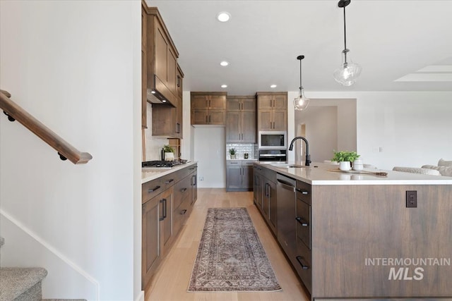 kitchen featuring a spacious island, sink, hanging light fixtures, stainless steel appliances, and backsplash