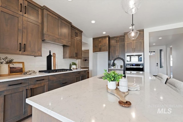 kitchen with decorative light fixtures, tasteful backsplash, sink, stainless steel appliances, and light stone countertops