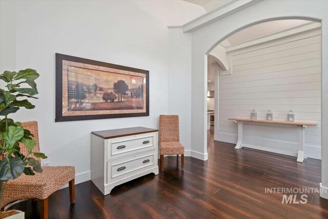 sitting room featuring baseboards, arched walkways, and dark wood finished floors