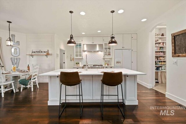 kitchen featuring glass insert cabinets, decorative light fixtures, light countertops, under cabinet range hood, and white fridge with ice dispenser