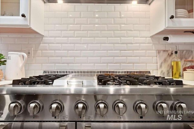 details featuring glass insert cabinets, stainless steel stove, white cabinetry, and tasteful backsplash