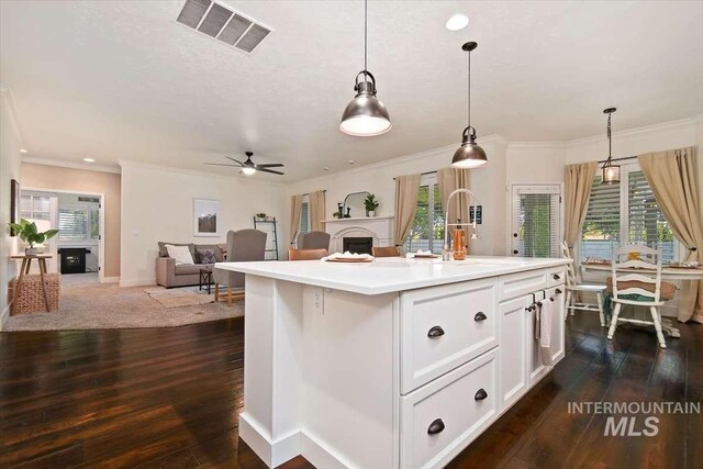 kitchen featuring light countertops, hanging light fixtures, visible vents, open floor plan, and an island with sink