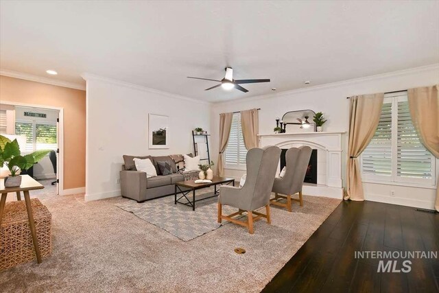 living room with a tile fireplace, wood finished floors, a ceiling fan, baseboards, and crown molding