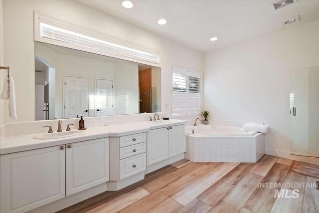 full bath with a garden tub, double vanity, a closet, a sink, and wood finished floors