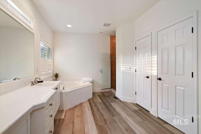 bathroom with vanity, a shower stall, a bath, and wood finished floors