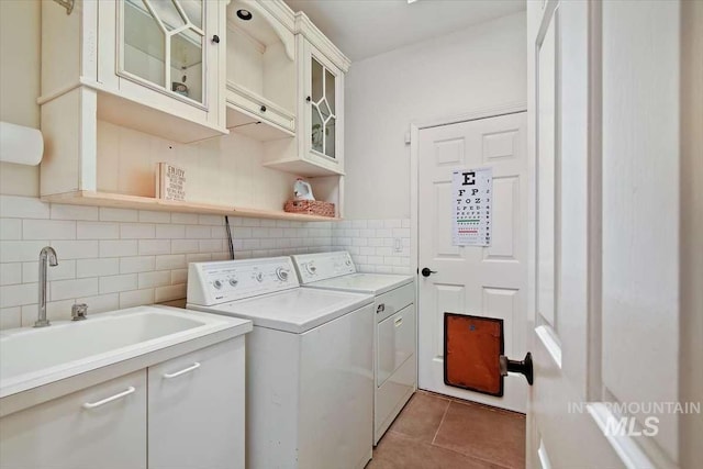 laundry room featuring tile walls, washing machine and clothes dryer, cabinet space, a sink, and dark tile patterned flooring