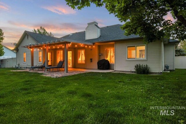 back of house featuring a pergola, a patio, a chimney, and a lawn