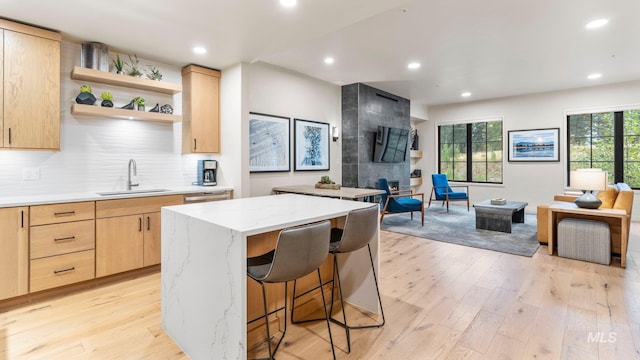 kitchen featuring a kitchen island, light brown cabinets, light hardwood / wood-style flooring, sink, and light stone counters