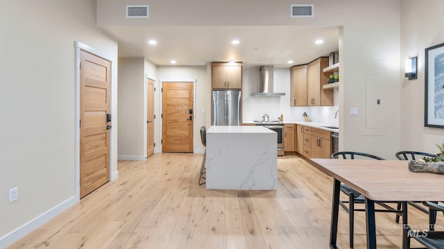 kitchen with wall chimney range hood, stainless steel appliances, a center island, light hardwood / wood-style floors, and tasteful backsplash