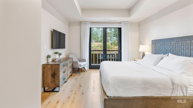 bedroom featuring access to exterior, light hardwood / wood-style flooring, and a tray ceiling