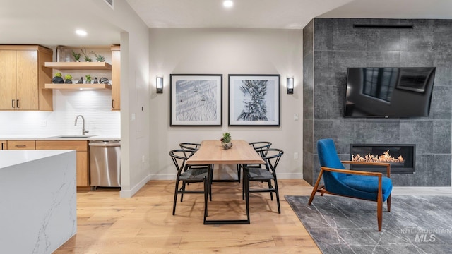 dining area with sink, a tiled fireplace, and light hardwood / wood-style floors