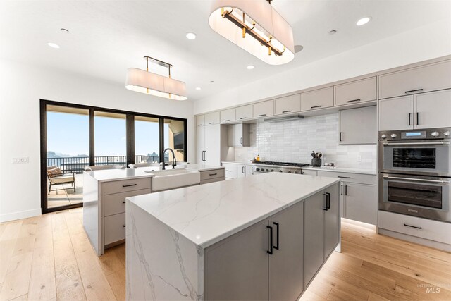 kitchen featuring sink, decorative light fixtures, gray cabinetry, and an island with sink