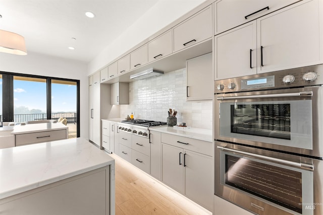 kitchen featuring appliances with stainless steel finishes, light hardwood / wood-style flooring, backsplash, and light stone countertops