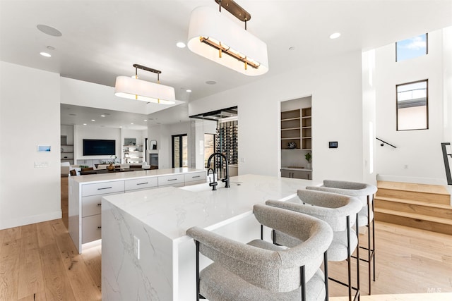 kitchen featuring decorative light fixtures, white cabinetry, light stone counters, light hardwood / wood-style floors, and a kitchen island with sink