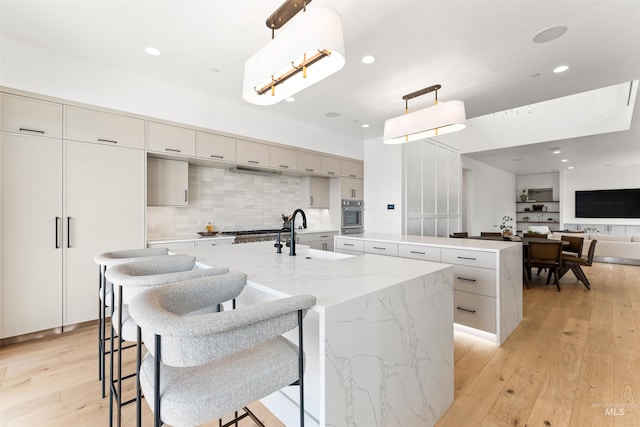 kitchen featuring stainless steel oven, light hardwood / wood-style flooring, decorative light fixtures, a center island with sink, and sink