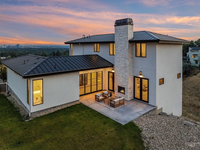 back house at dusk with an outdoor living space with a fireplace, a patio area, and a yard