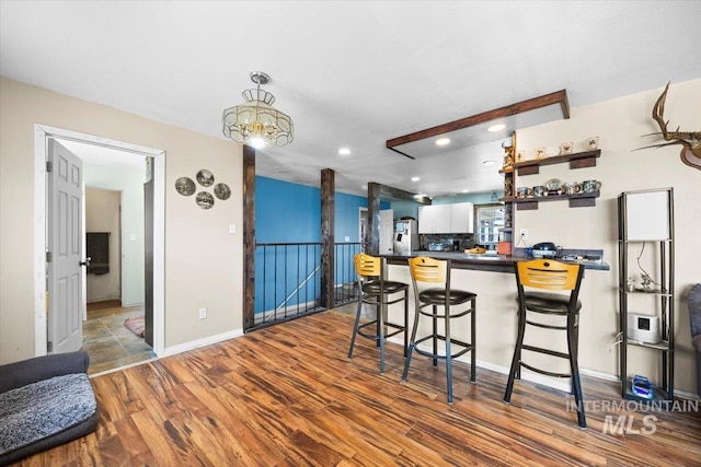 kitchen with kitchen peninsula, a kitchen breakfast bar, wood-type flooring, backsplash, and white cabinets