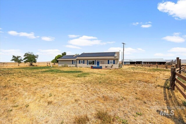 back of house featuring a lawn, a rural view, and solar panels