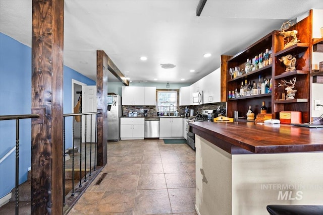 kitchen with butcher block counters, appliances with stainless steel finishes, tasteful backsplash, white cabinetry, and sink