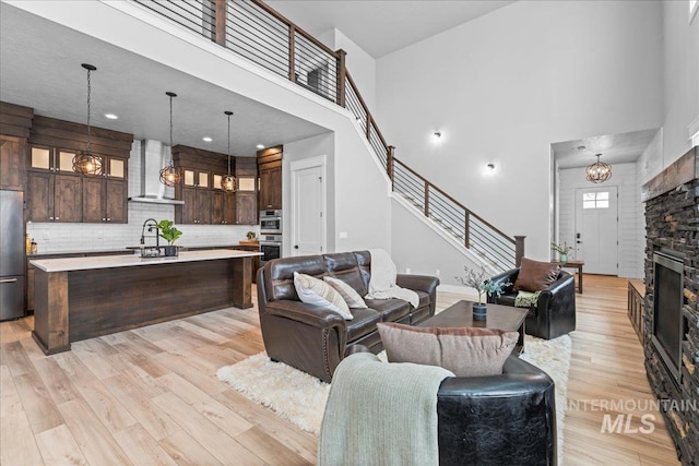 living room featuring light wood finished floors, a fireplace, stairs, and a high ceiling