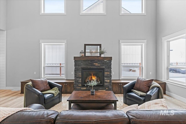 living area featuring a stone fireplace, a high ceiling, baseboards, and wood finished floors