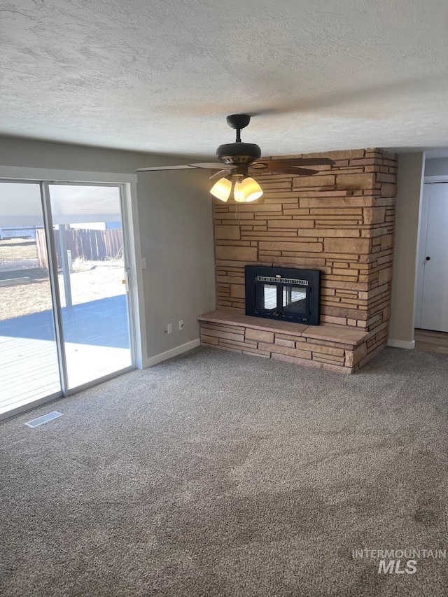 unfurnished living room with ceiling fan, a fireplace, a textured ceiling, and carpet flooring