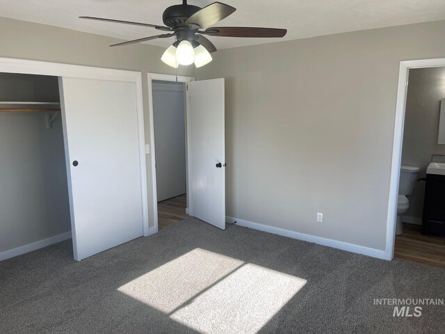 unfurnished bedroom featuring ceiling fan, a closet, ensuite bath, and dark colored carpet