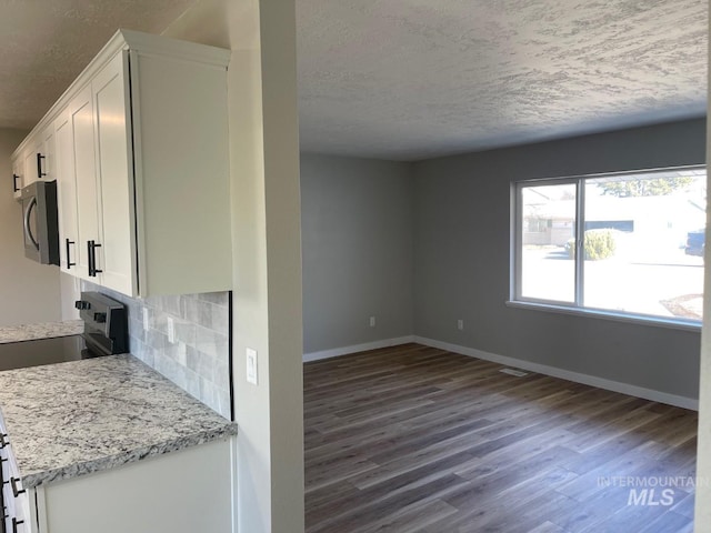 kitchen featuring backsplash, stainless steel appliances, light stone countertops, a textured ceiling, and white cabinets