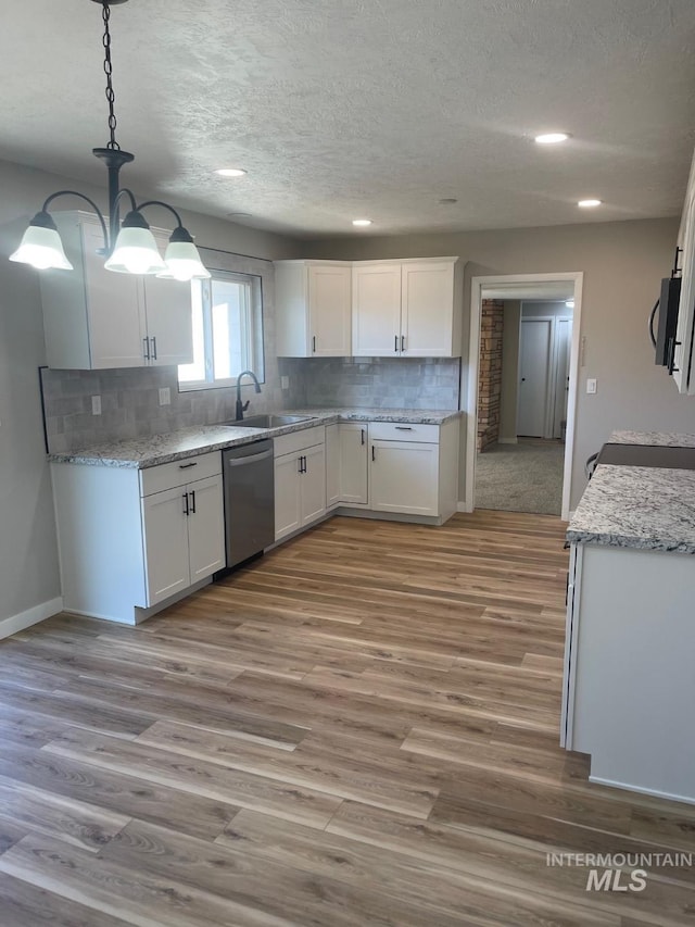 kitchen featuring dishwasher, sink, white cabinets, hanging light fixtures, and light hardwood / wood-style flooring