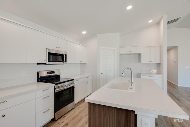 kitchen with stainless steel appliances, a center island with sink, light hardwood / wood-style floors, white cabinetry, and lofted ceiling