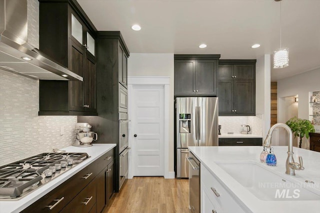 kitchen featuring white cabinetry, sink, wall chimney exhaust hood, stainless steel appliances, and pendant lighting