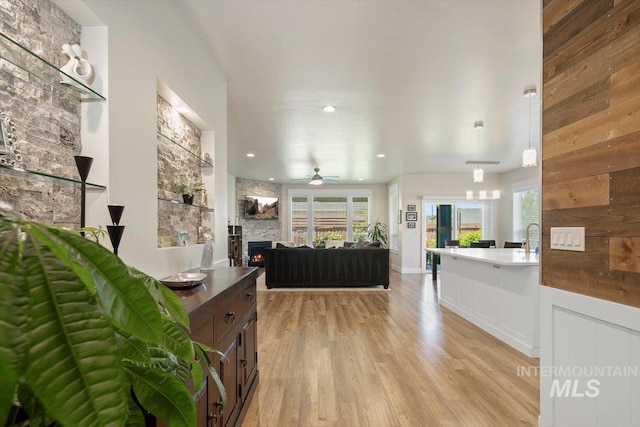 living room featuring a fireplace, light wood-type flooring, ceiling fan, and wooden walls