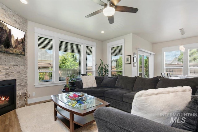 living room with hardwood / wood-style flooring, a stone fireplace, a wealth of natural light, and ceiling fan