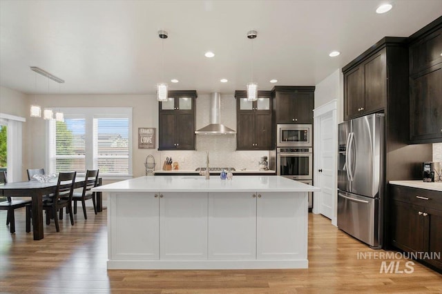 kitchen featuring dark brown cabinetry, stainless steel appliances, a kitchen island with sink, and wall chimney range hood