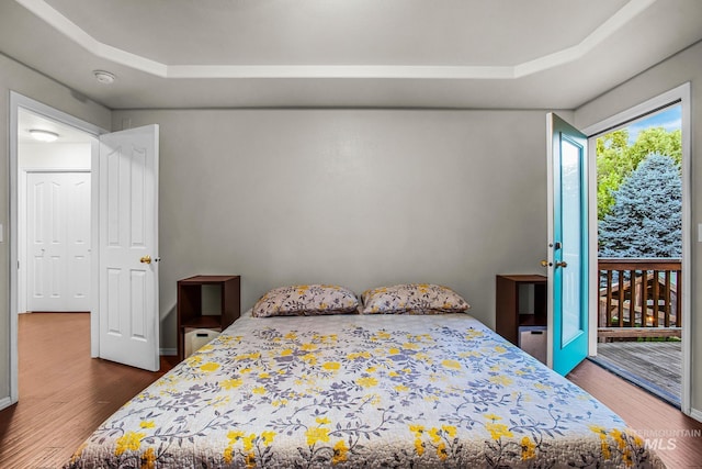 bedroom featuring dark hardwood / wood-style floors, access to outside, and a tray ceiling