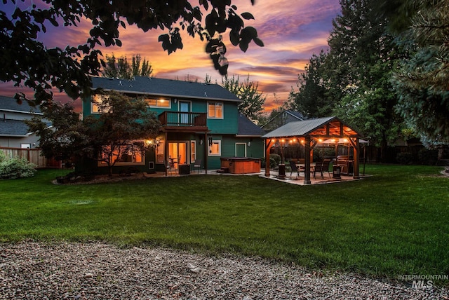 back house at dusk featuring a lawn, a patio area, a balcony, and a hot tub