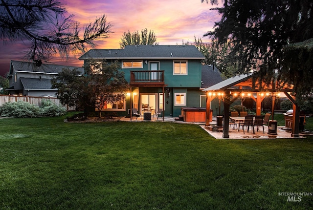 back house at dusk featuring a lawn, a patio area, a balcony, and a hot tub