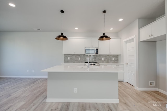 kitchen featuring pendant lighting, white cabinetry, a kitchen island with sink, and decorative backsplash