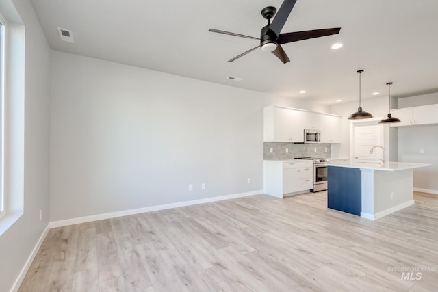 kitchen featuring white cabinetry, hanging light fixtures, stainless steel appliances, an island with sink, and decorative backsplash