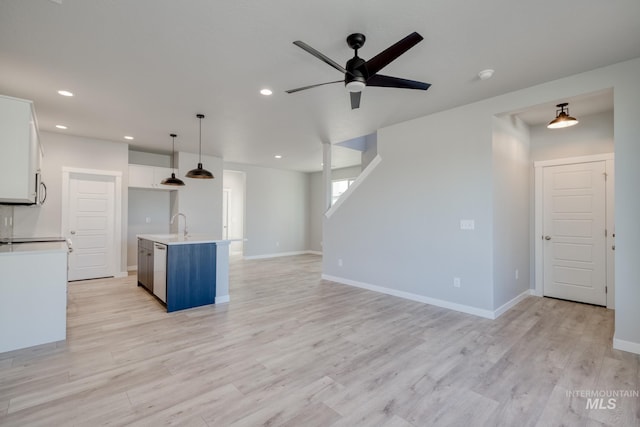 kitchen with decorative light fixtures, white cabinets, ceiling fan, a center island with sink, and light wood-type flooring