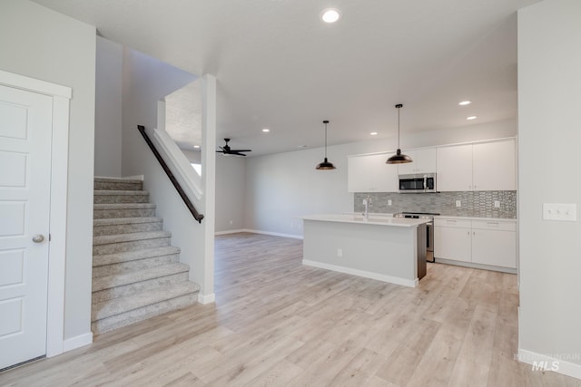 kitchen with light wood-type flooring, appliances with stainless steel finishes, pendant lighting, decorative backsplash, and white cabinets