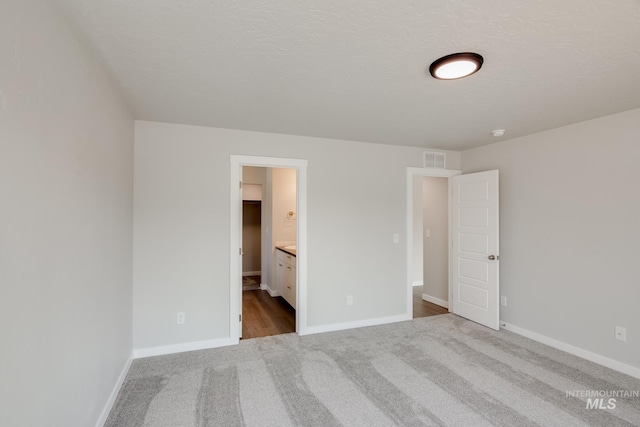 unfurnished bedroom featuring ensuite bath, a spacious closet, light colored carpet, and a textured ceiling