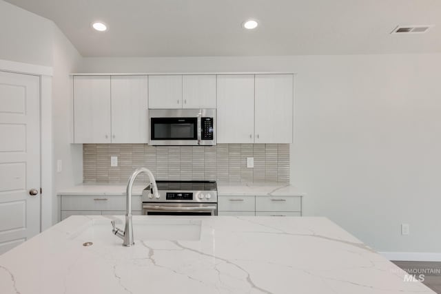 kitchen with appliances with stainless steel finishes, light stone countertops, decorative backsplash, and white cabinets